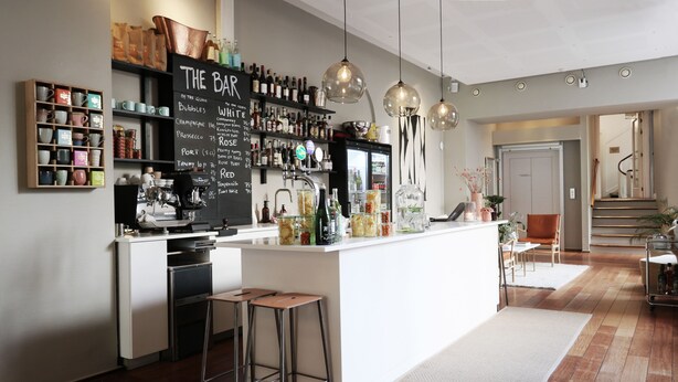 A modern kitchen with a bar area, wooden stools, and a chalkboard menu listing beverages.