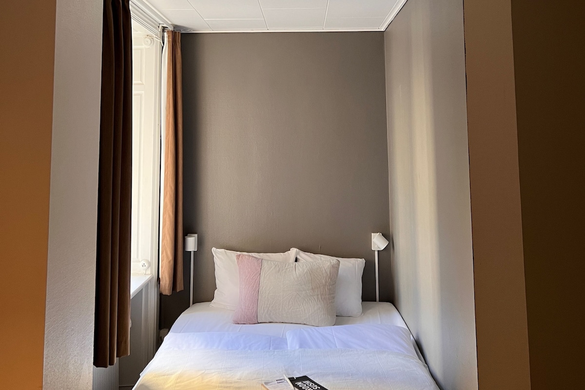 A hotel room with a bed, a ceiling light, and a window with curtains.