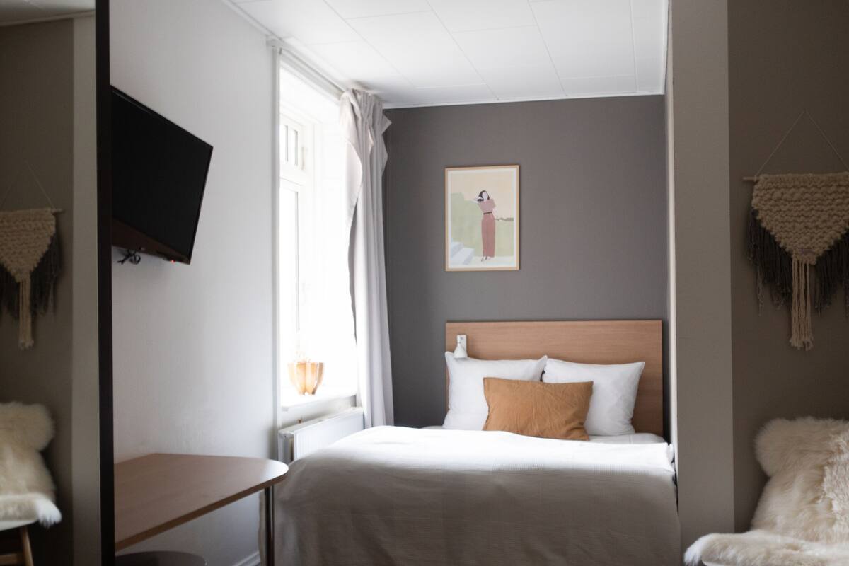 A hotel room with a bed, a desk, a chair, a television, and a window with curtains.
