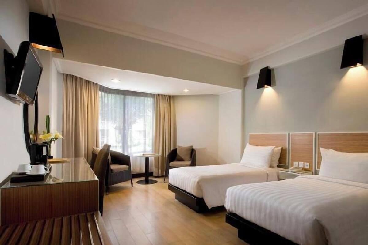 Habitación de hotel con escritorio, dos camas, televisor y ventana con cortinas.