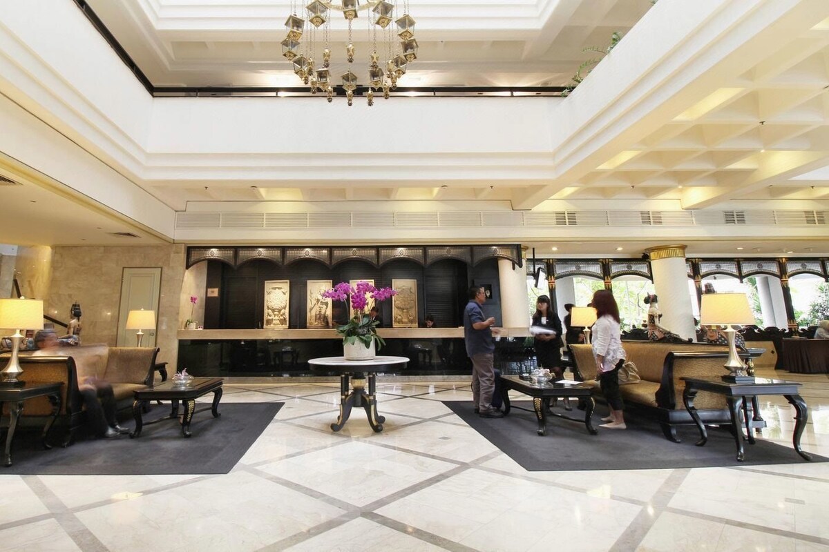 A hotel lobby with a central reception desk, seating areas, and a chandelier.