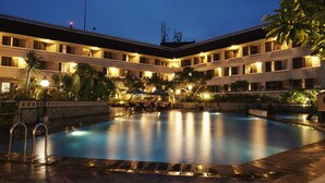 A hotel courtyard with a swimming pool, outdoor seating, and lush greenery.