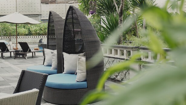 Outdoor seating with cushions, a pool area, and surrounding greenery.
