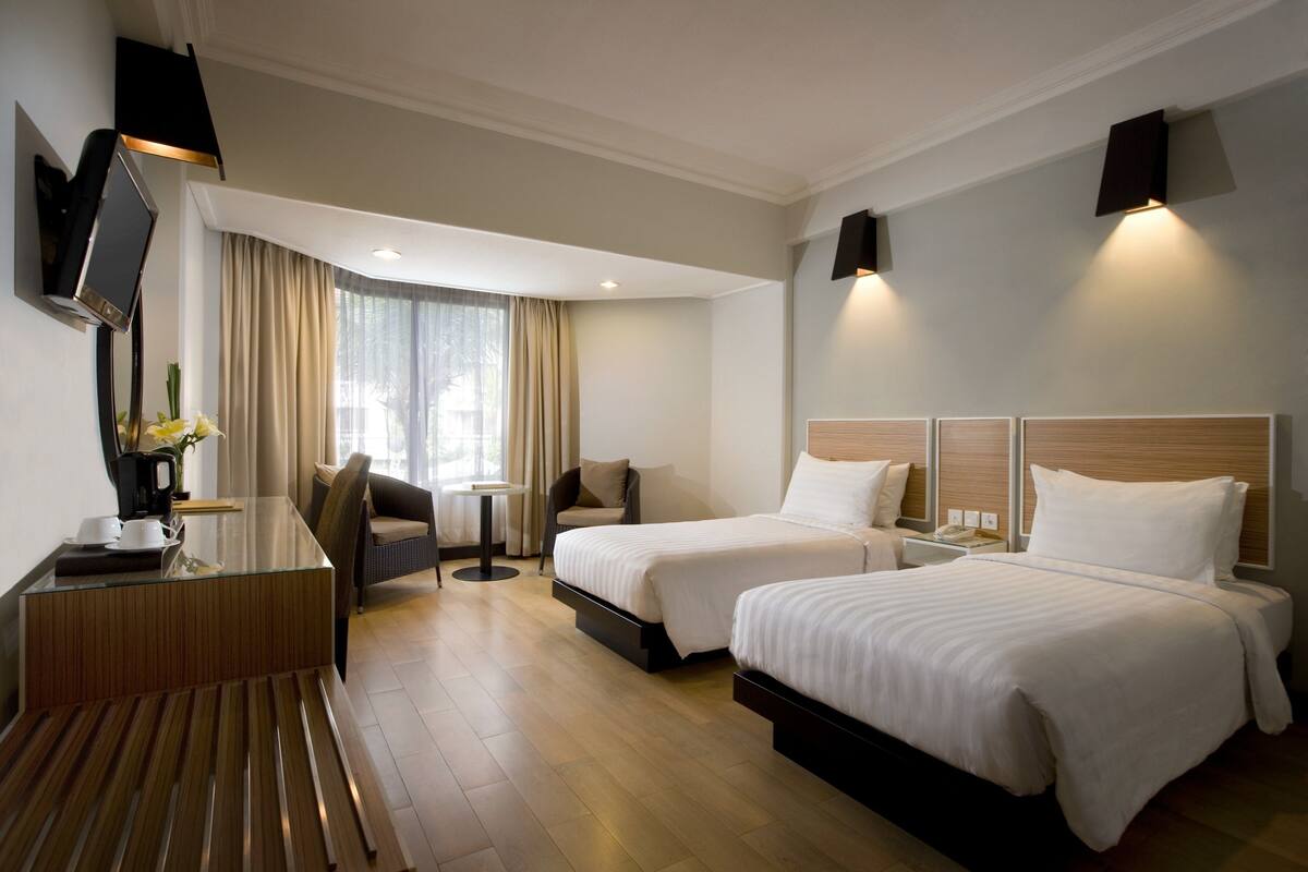 Habitación de hotel con dos camas, un escritorio con silla, una mesita y un televisor montado en la pared.