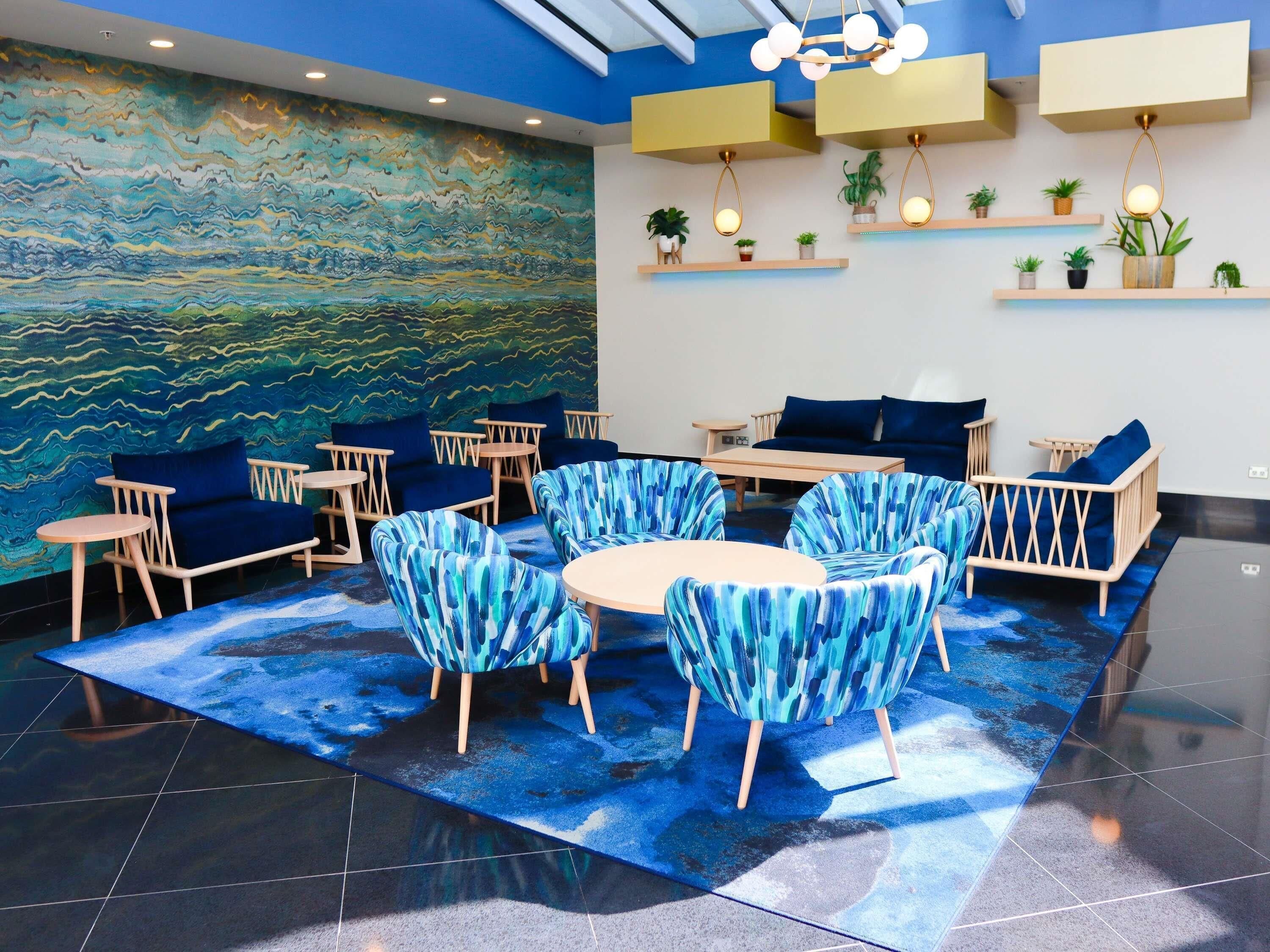A modern lounge area with blue-themed furniture, a large abstract mural, and built-in shelves with plants.