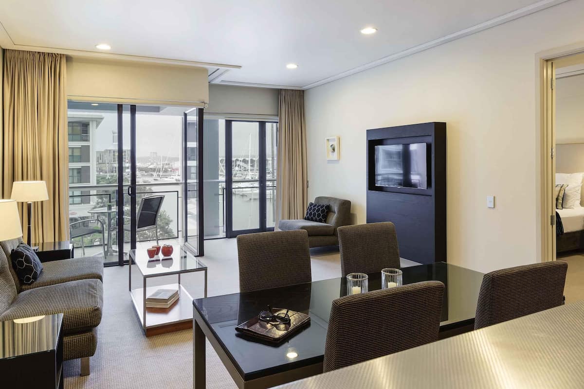 A modern hotel room with a balcony, a flat-screen TV, a dining table, and a sofa.