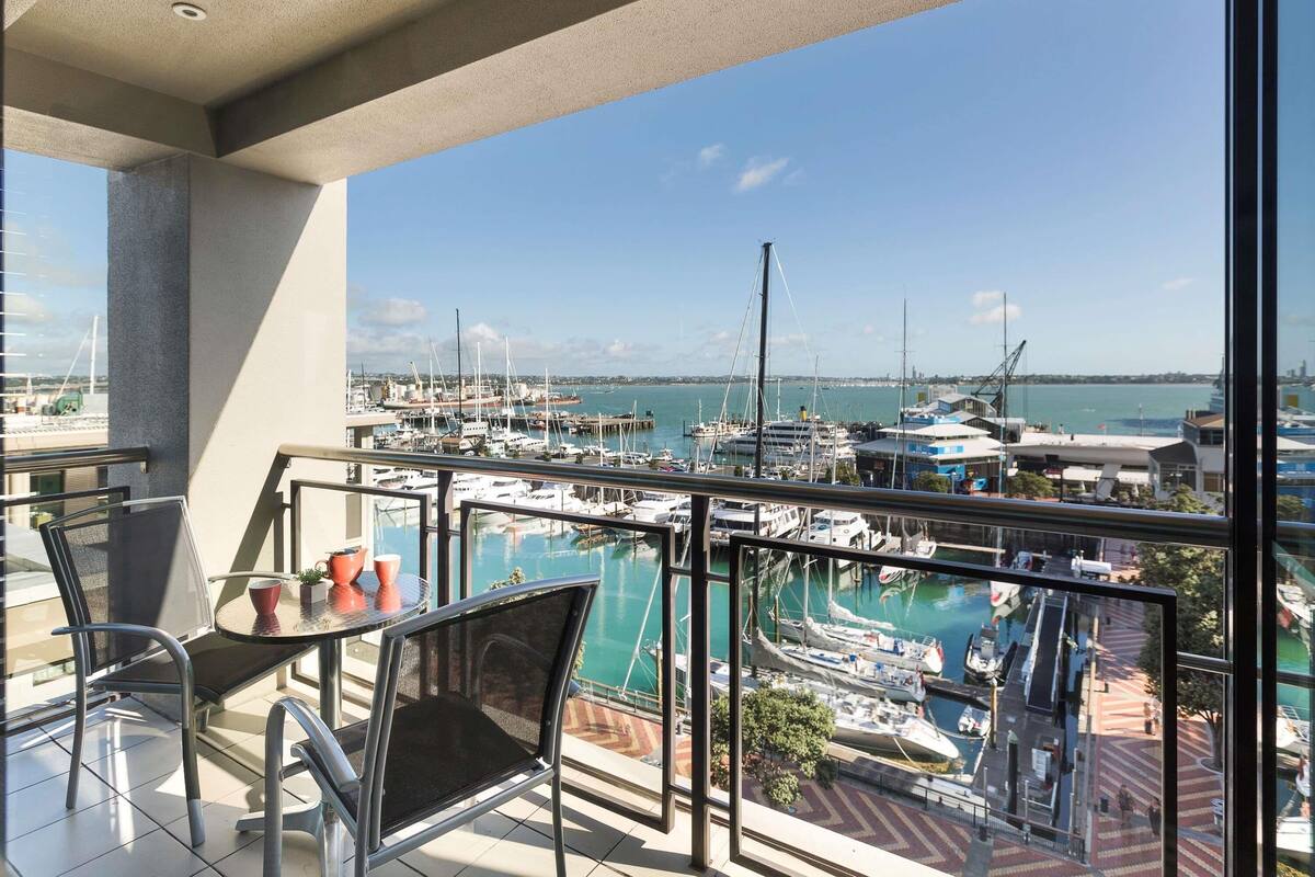 A balcony with a view of a marina, chairs, a table, and a glass railing.