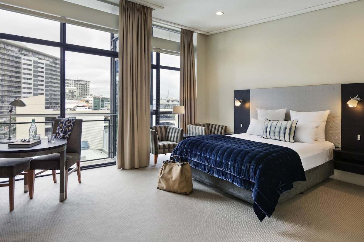 A hotel room with a large bed, a desk with a chair, a window with curtains, and a view of the cityscape.