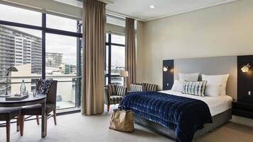 A hotel room with a large bed, a desk with a chair, a window with curtains, and a view of the cityscape.