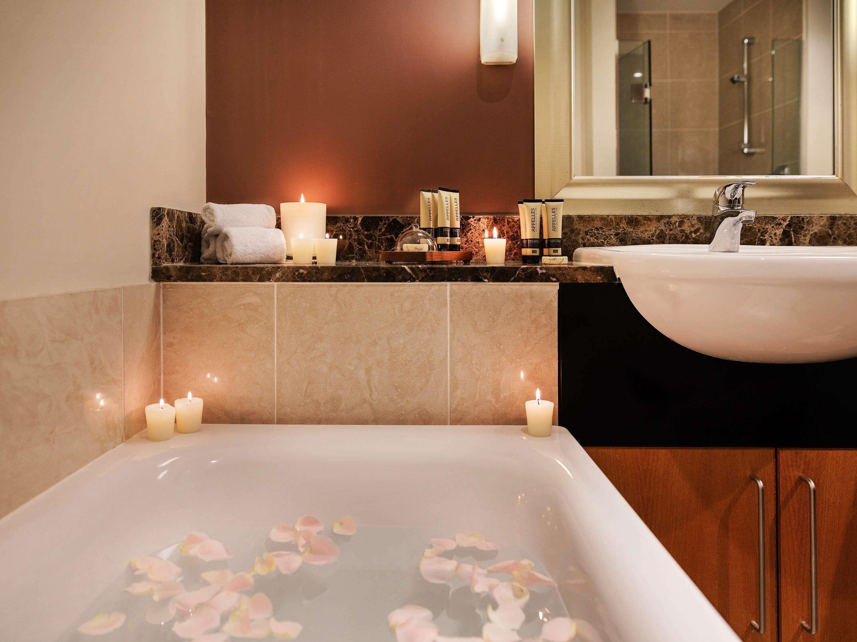 A bathroom with a bathtub filled with rose petals, a sink, and candles on the counter.