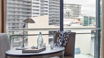 A balcony with a view of a cityscape, a table with a lamp, glasses, and a bottle.