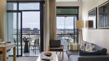 Un salon moderne comprenant un canapé, un fauteuil, une table à manger et offrant une vue sur le port de plaisance grâce à de grandes fenêtres.