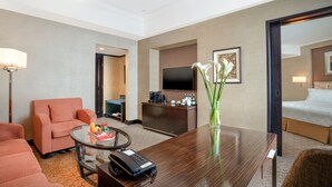 Ein Hotelzimmer mit einem Bett, einem Schreibtisch mit Telefon, einem Fernseher, einer Couch und einer Vase mit Blumen.