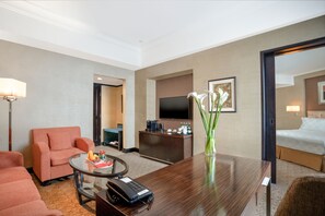 Ein Hotelzimmer mit einem Bett, einem Schreibtisch mit Telefon, einem Fernseher, einer Couch und einer Vase mit Blumen.