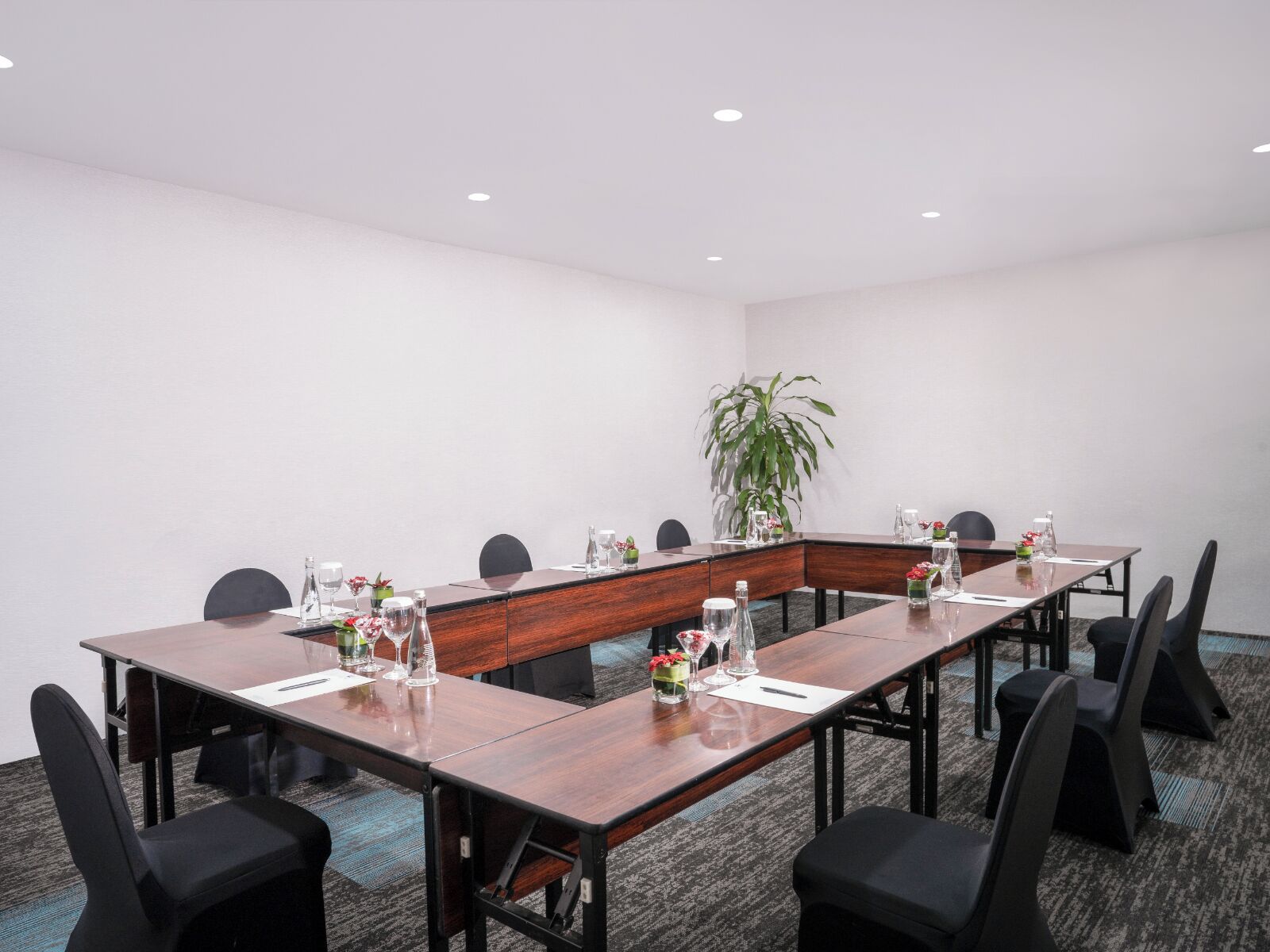 Un salón de conferencias con una larga mesa, sillas negras y una planta en maceta.