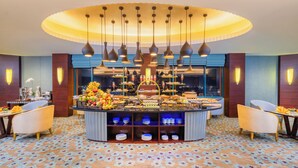 Ein Hotel-Frühstücksbereich mit einem zentralen Buffet, verschiedenen Sitzmöglichkeiten und einem gemusterten Boden.