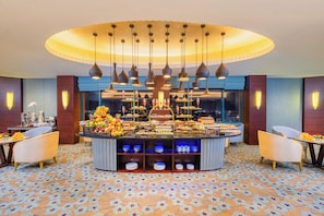 Ein Hotel-Frühstücksbereich mit einem zentralen Buffet, verschiedenen Sitzmöglichkeiten und einem gemusterten Boden.