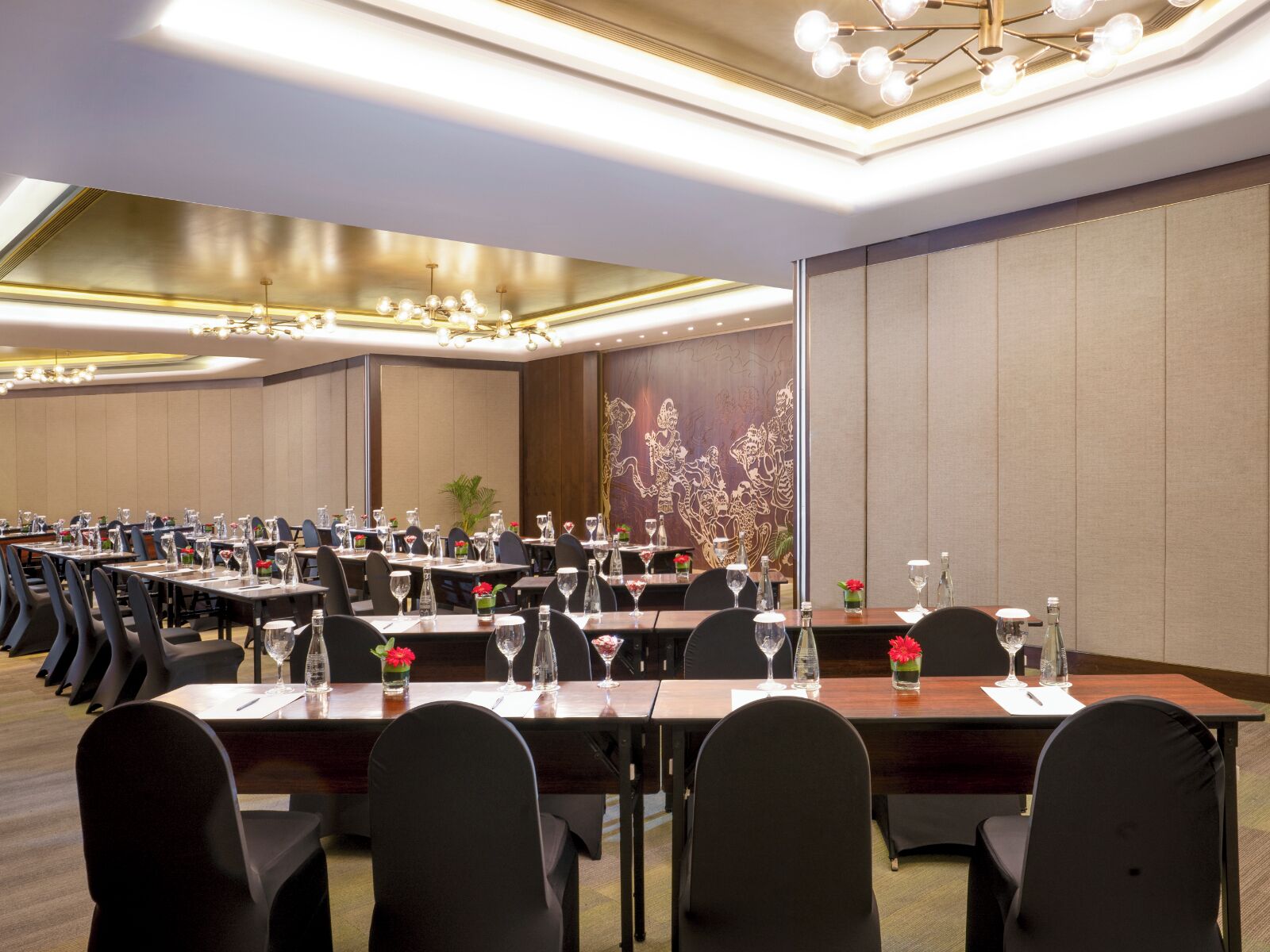A conference room with multiple tables and chairs, equipped with water glasses and red flowers.