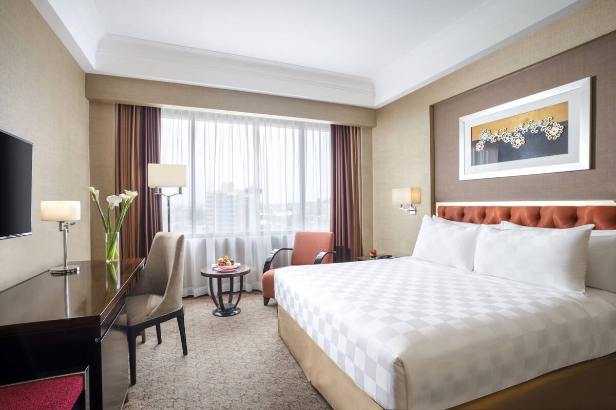 Ein Hotelzimmer mit einem großen Bett, einem Schreibtisch mit Stuhl, einem kleinen Tisch mit Lampe und einem Fernseher an der Wand.