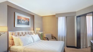 A hotel room with a large bed, a desk, a chair, a lamp, and a window with curtains. - Hotel Ciputra Semarang (Semarang)