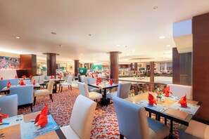 A spacious indoor dining area with multiple tables and chairs, a patterned carpet, and a view of the dining area through a glass partition. - Hotel Ciputra Semarang (Semarang)