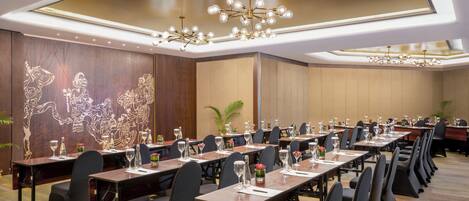 Un salón de conferencias con mesas largas, sillas y un techo con candelabros.