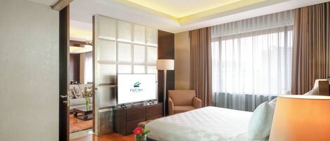 A hotel room with a bed, a desk, a chair, a TV, and a window with curtains.