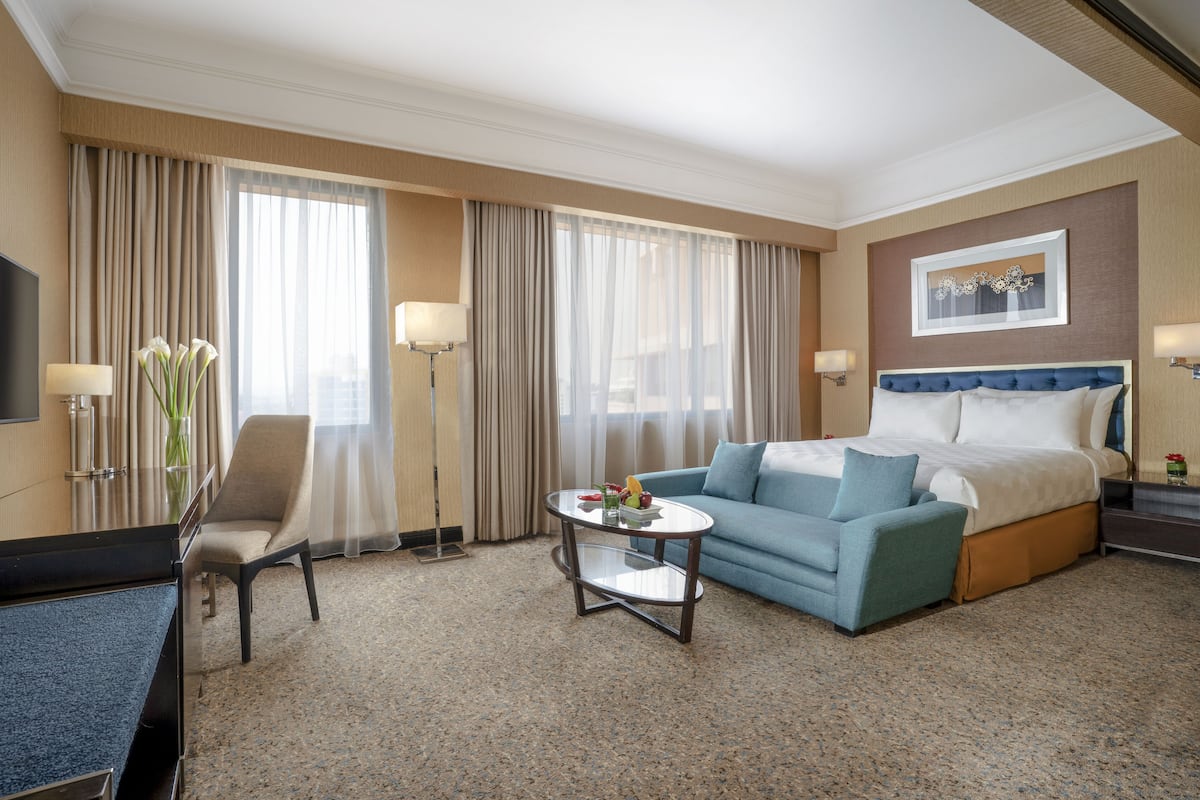 Ein Hotelzimmer mit Bett, Sofa, Sessel, Couchtisch und Fernseher.