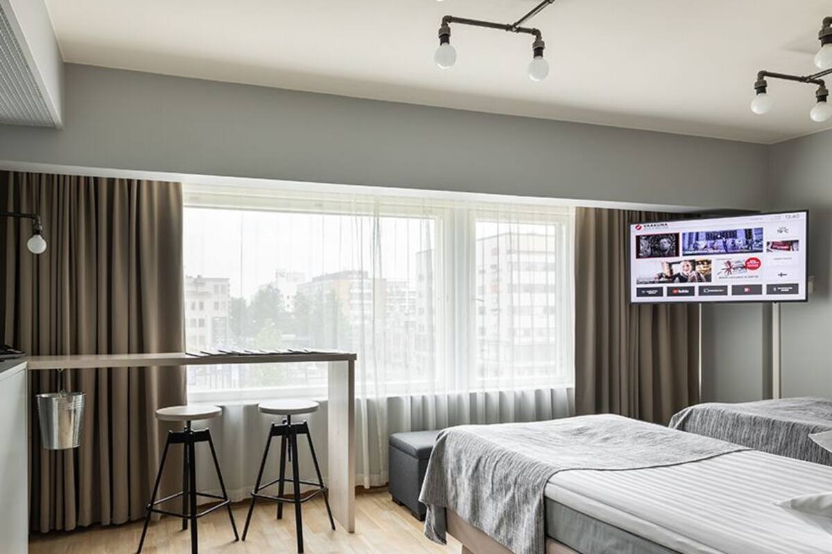 Ein modernes Hotelzimmer mit Schreibtisch, zwei Barhocker, einem Bett und einem Fernseher.