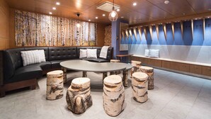 Un'area lounge moderna con un divano in pelle nera, un tavolino rotondo e sgabelli in legno di betulla.