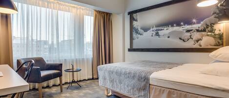 A hotel room with a bed, a chair, a table, and a large window with curtains.
