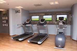 Ein Fitnessraum mit Laufbändern, Crosstrainern und einem an der Wand montierten Fernseher.