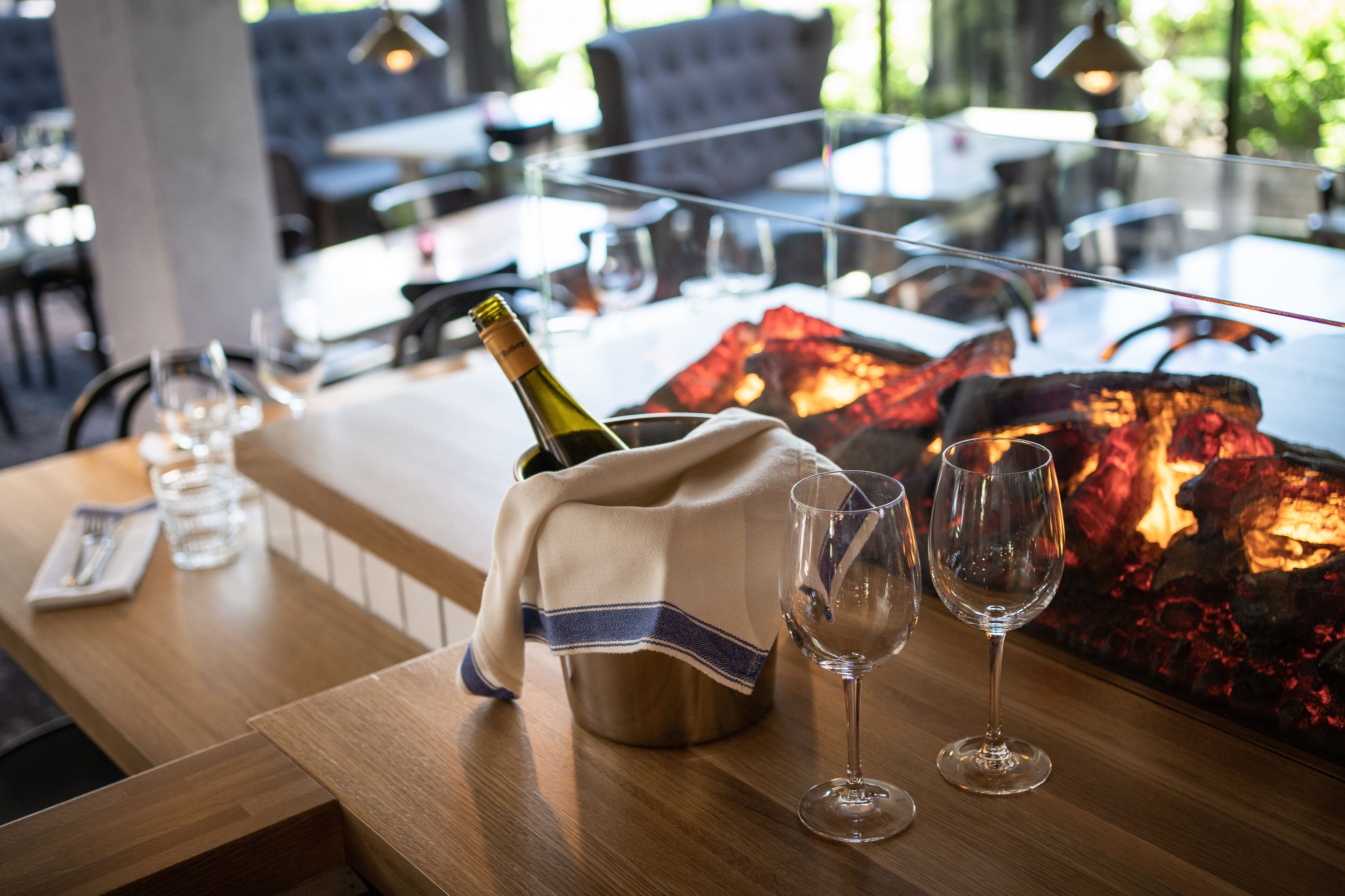 A restaurant setting with a table set for two, a bottle of champagne, and two glasses.