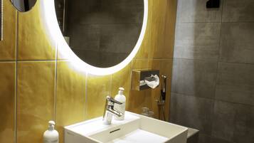 A modern bathroom with a white sink, a mirror with a circular light, and a towel rack.