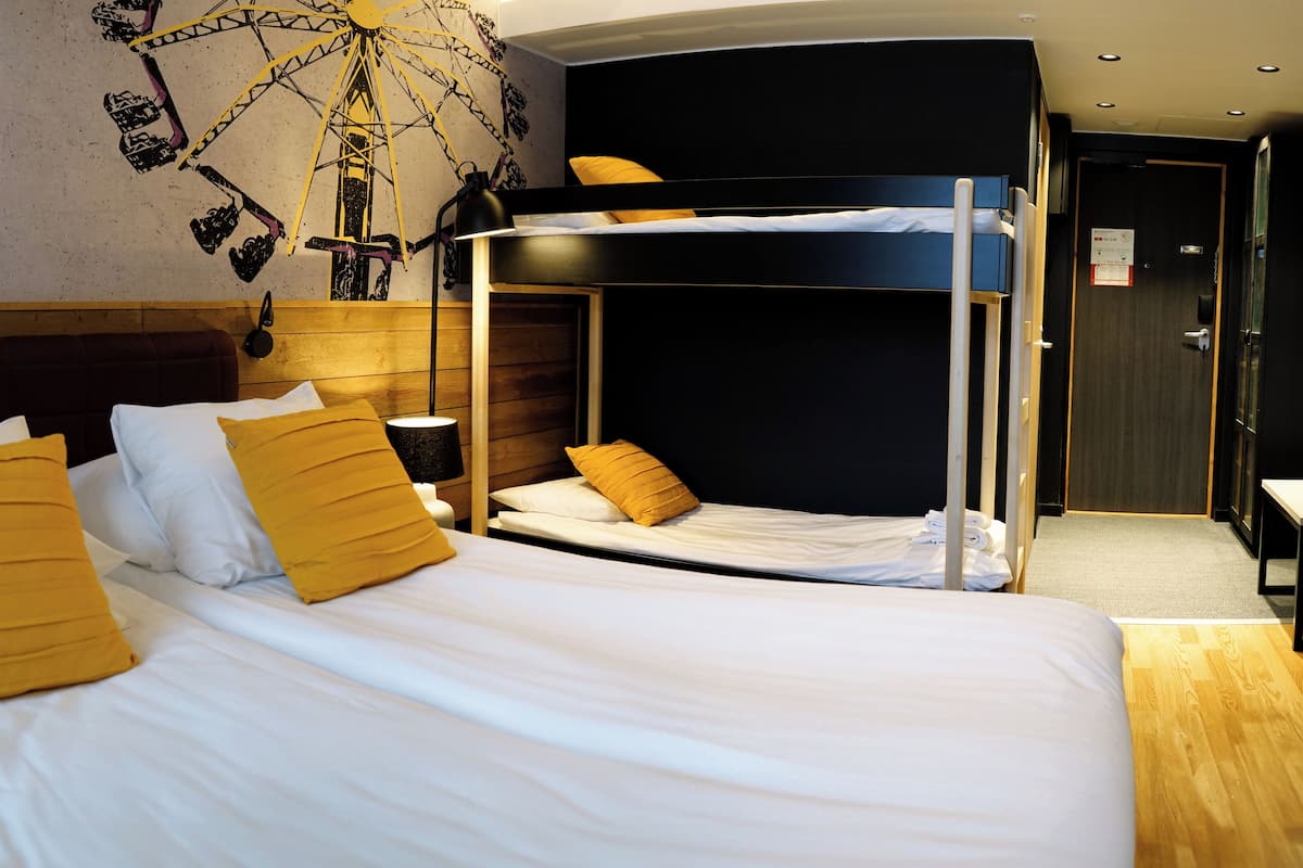 A hotel room with a bunk bed, a desk, and a wall-mounted lamp.