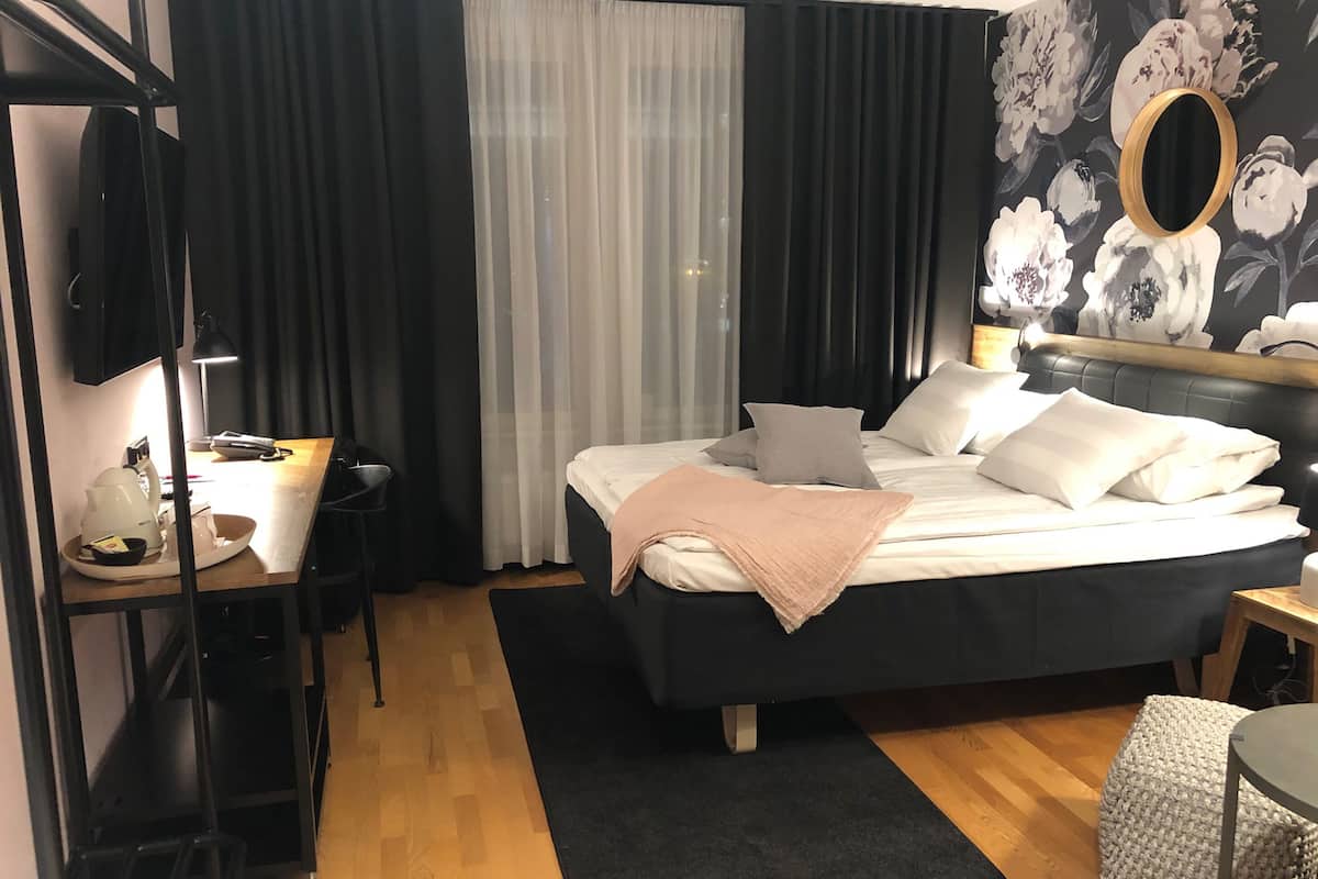 A hotel room with a bed, bedside table, lamp, and a mirror.