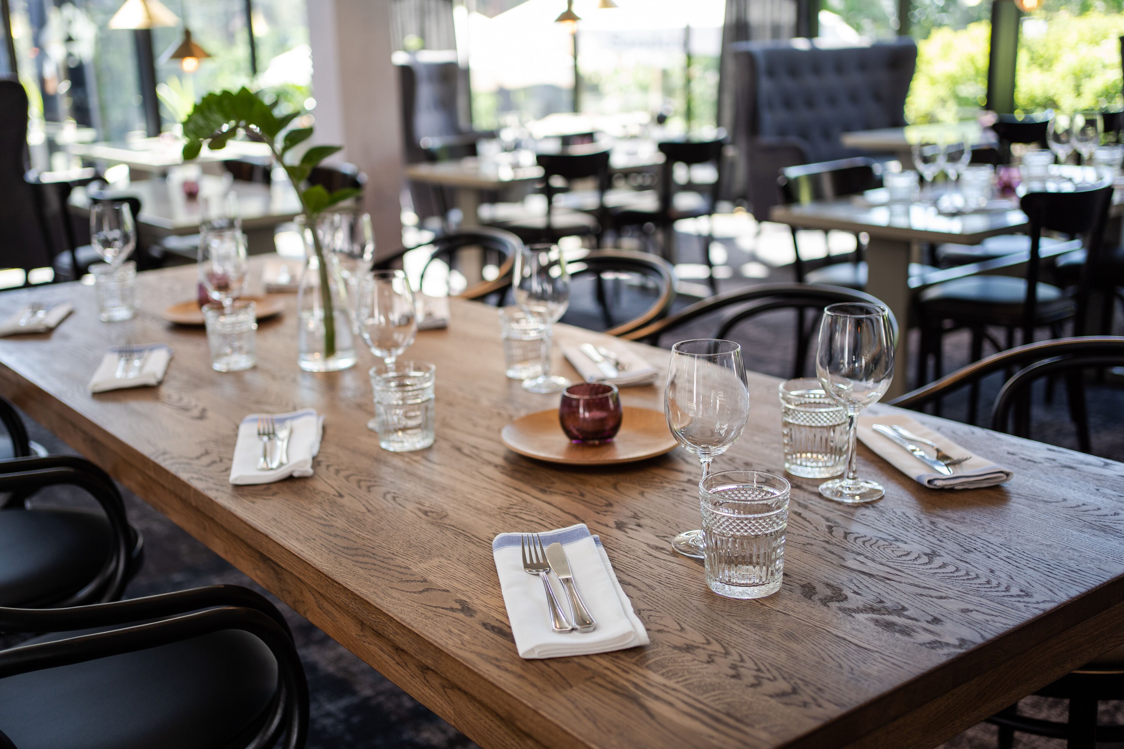 A restaurant dining area with wooden tables, chairs, and neatly set tables with cutlery and glasses.