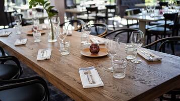 A restaurant dining area with wooden tables, chairs, and neatly set tables with cutlery and glasses.