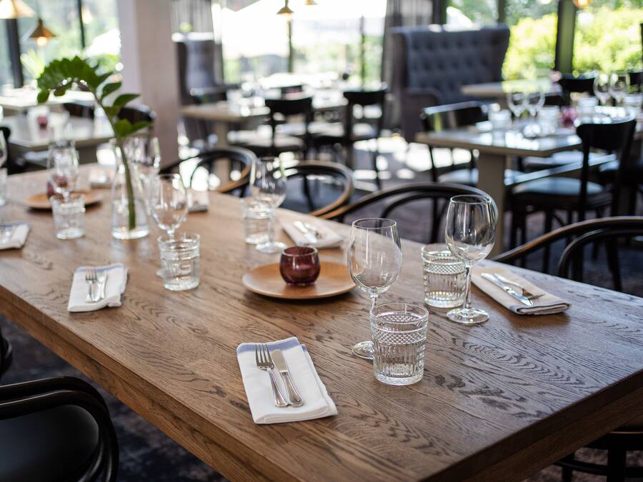 A restaurant dining area with wooden tables, chairs, and neatly set tables with cutlery and glasses.