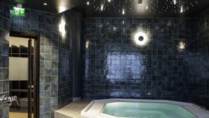 Um banheiro moderno com banheira independente, paredes com azulejos escuros e área de chuveiro aparente.