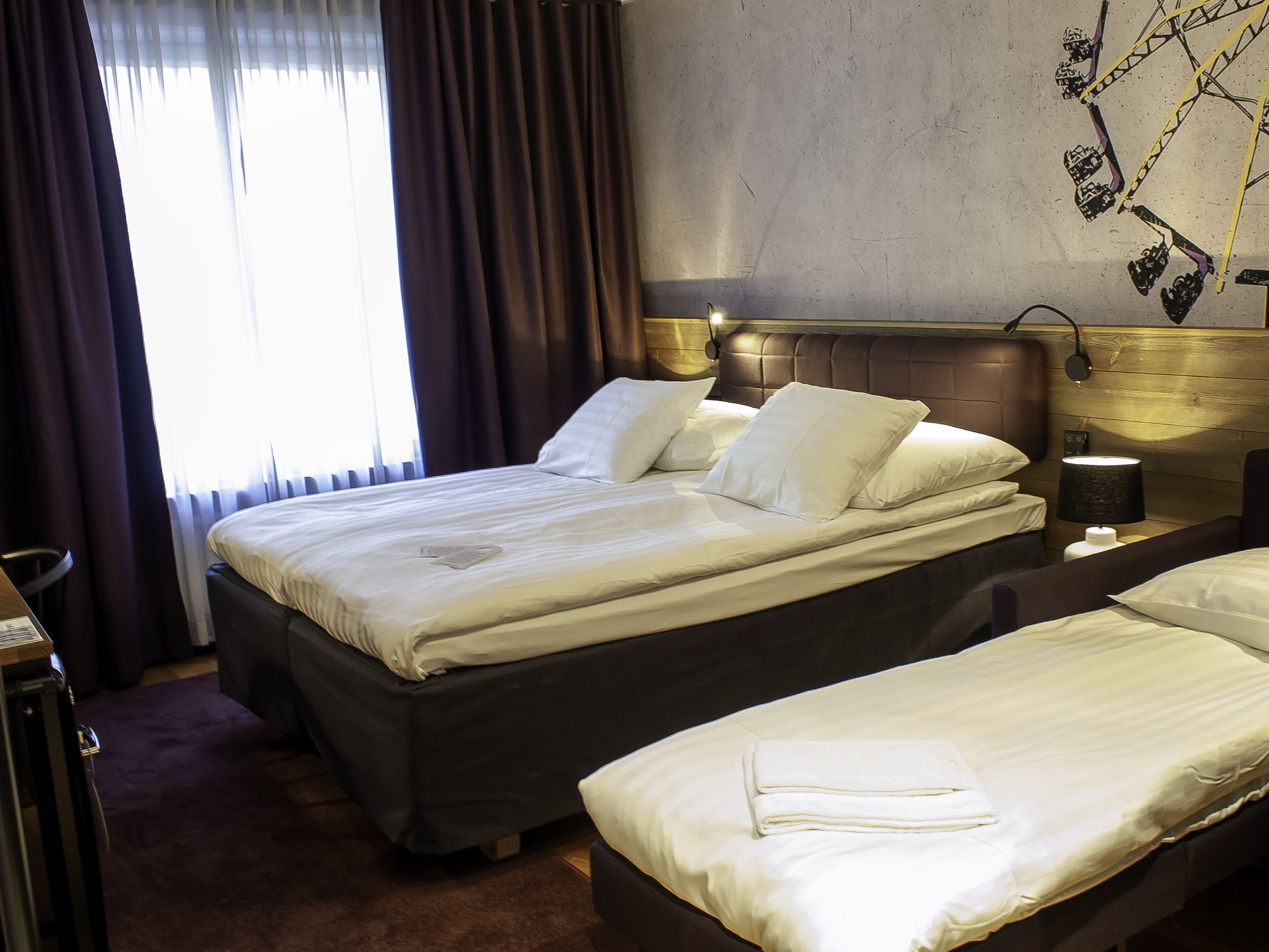 A hotel room with two beds, a nightstand, a lamp, and a window with curtains.