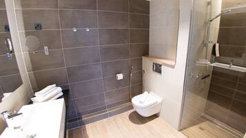 A modern bathroom with a glass-enclosed shower, a white toilet, and a sink with a mirror.