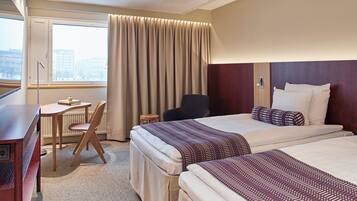 A hotel room with two beds, a desk, a chair, and a view of the city.