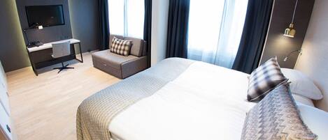 A hotel room with a large bed, a desk with a chair, a television, and a sofa.