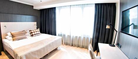 A modern hotel room with a large bed, a desk, and a TV.