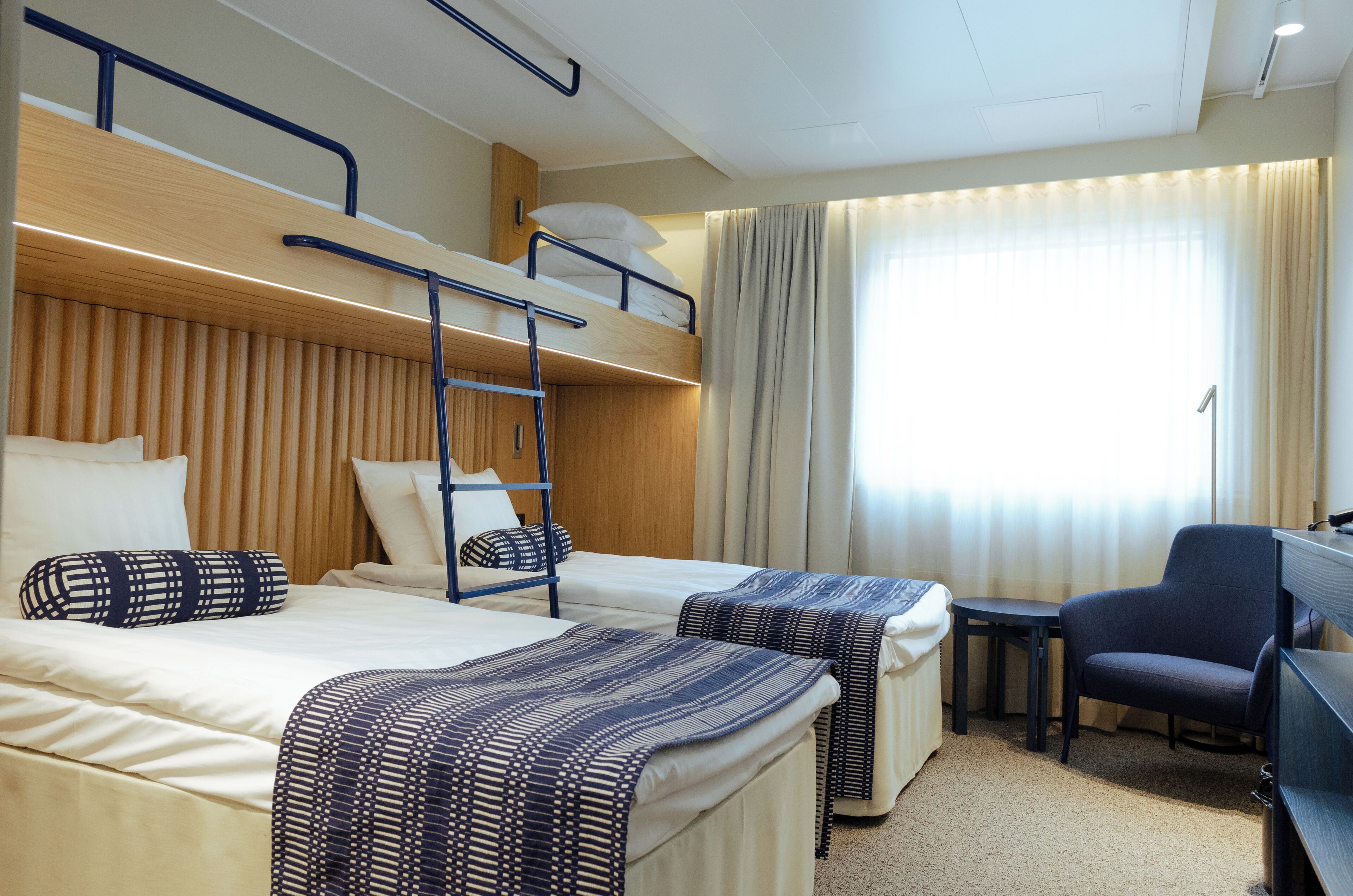 A hotel room with bunk beds, a desk, a chair, and a window with curtains.