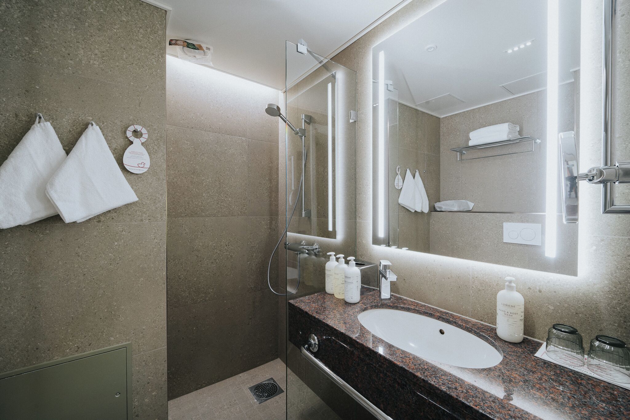 Un baño moderno con ducha de vidrio, encimera de granito y un espejo grande.