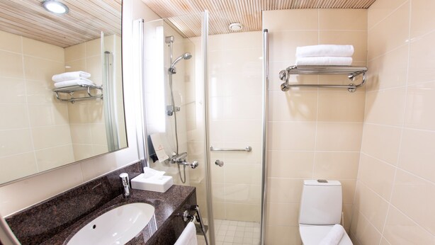 A bathroom with a granite countertop sink, a glass shower enclosure, and a toilet. - Original Sokos Hotel Alexandra (Jyväskylä)