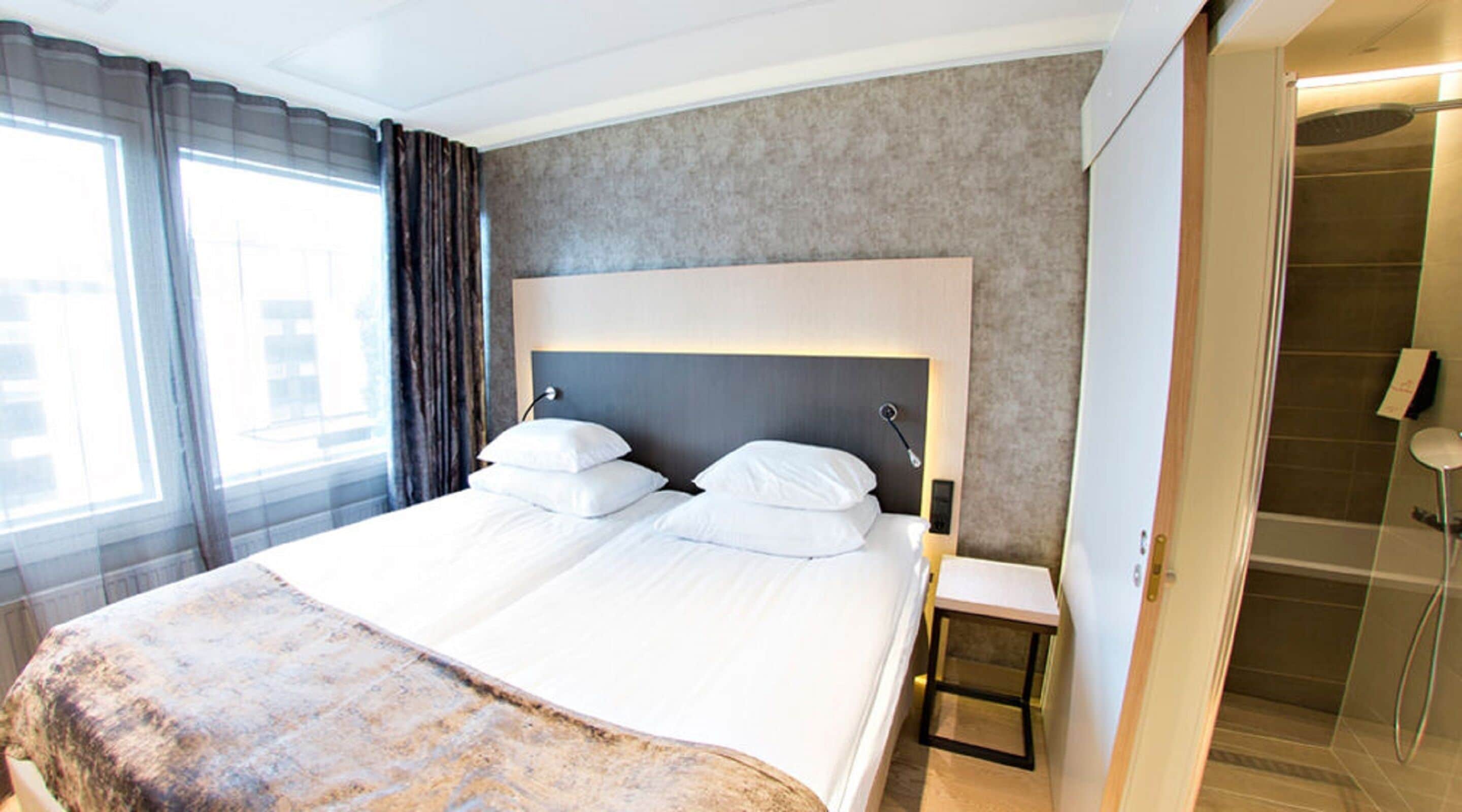 Habitación de hotel con una cama grande, una mesita de noche, zona de ducha y vistas al exterior por la ventana.