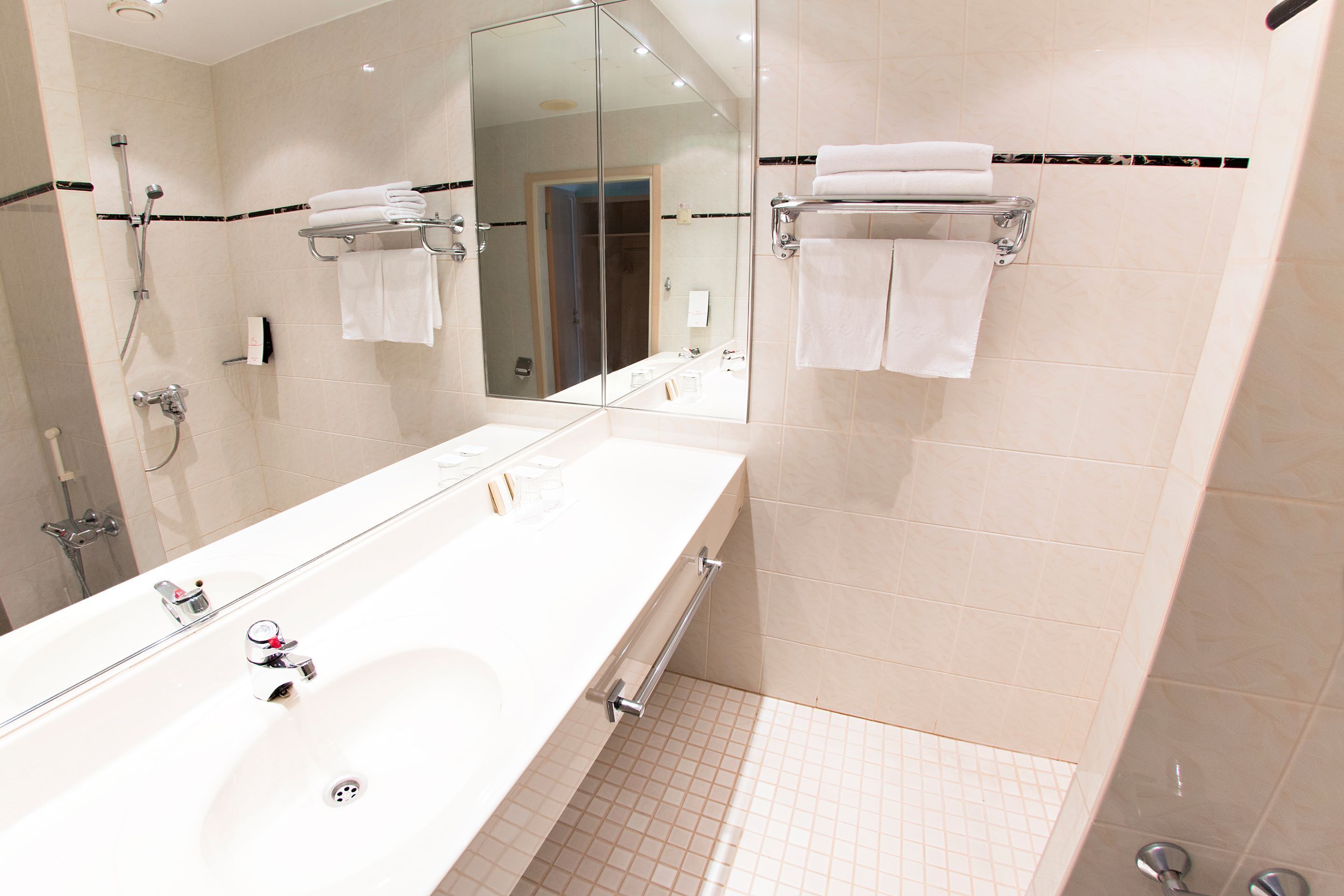A modern bathroom with a large mirror, a white sink, and a shower area.